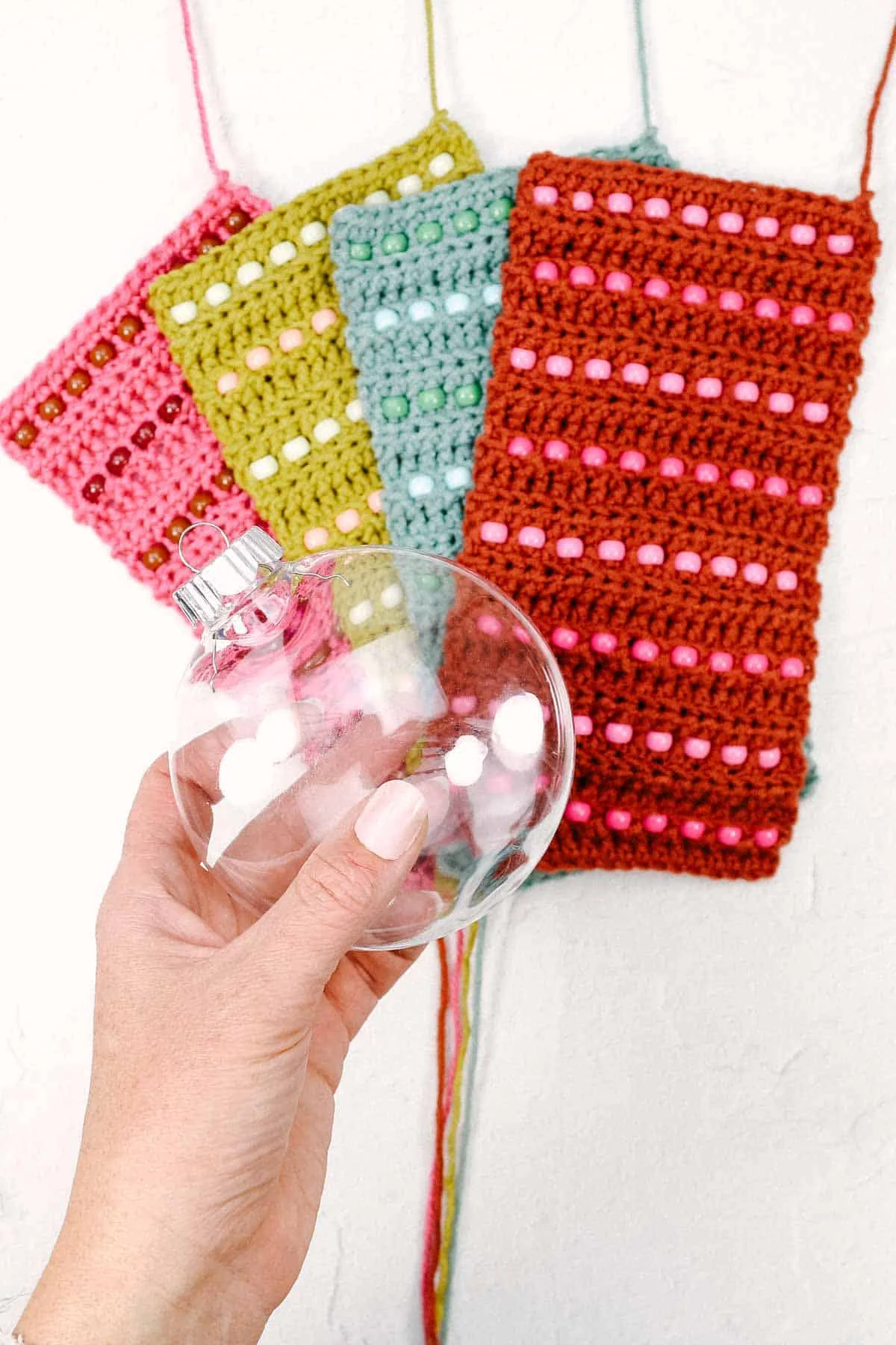 Four in-progress crochet baubles with pony beads and a woman holding a plastic bauble ornament.