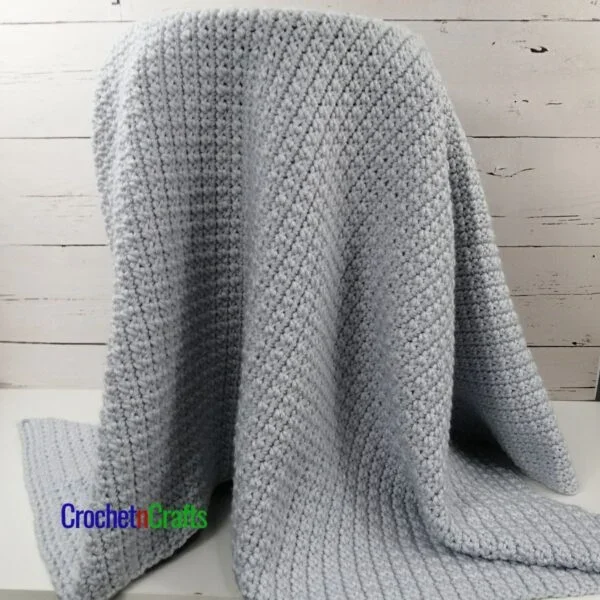 Cozy crochet lapghan draped over a stool.