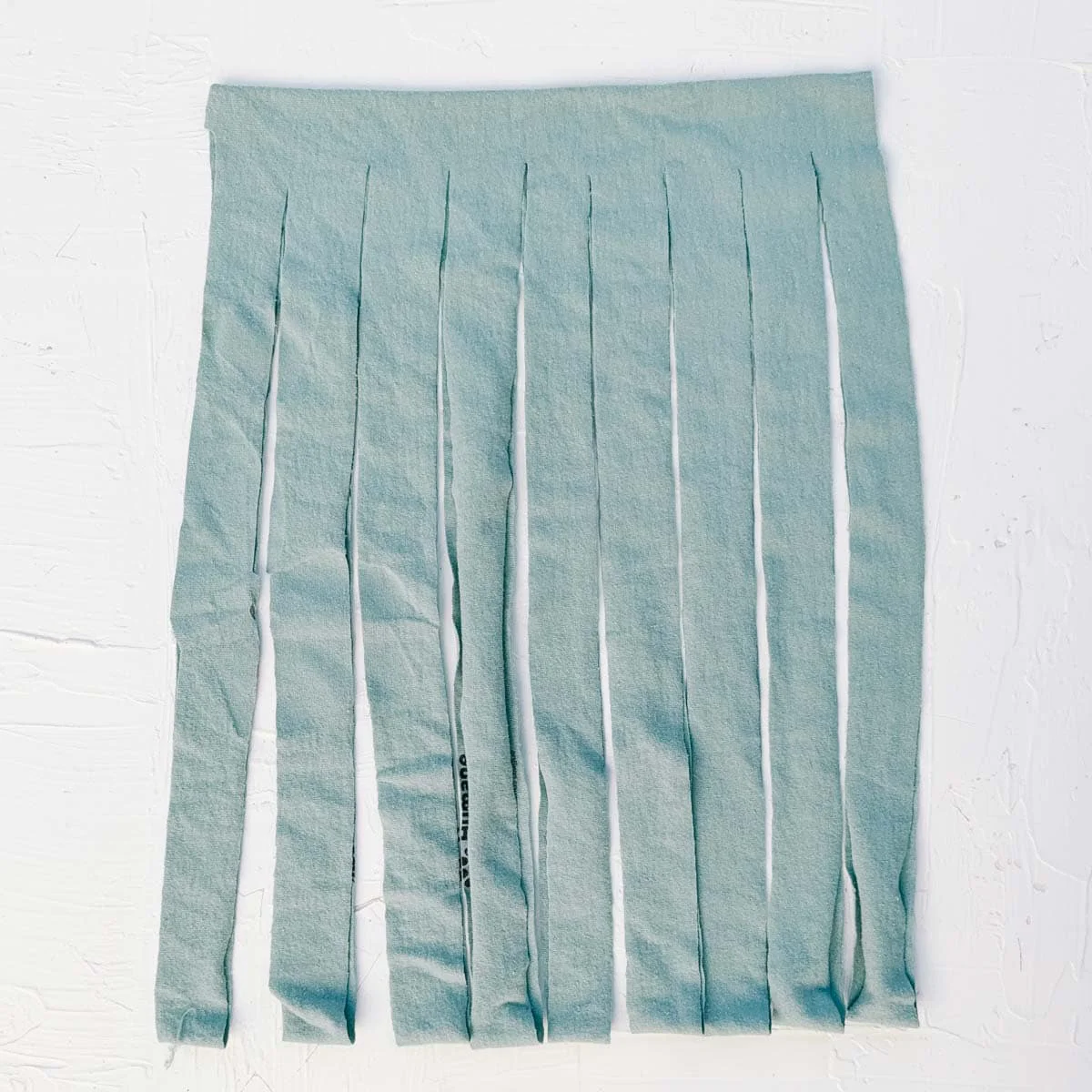 A blue t-shirt cut into fringed strips in the process of creating t-shirt yarn.