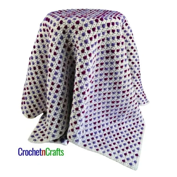 A crocheted lapghan draped over a stool.