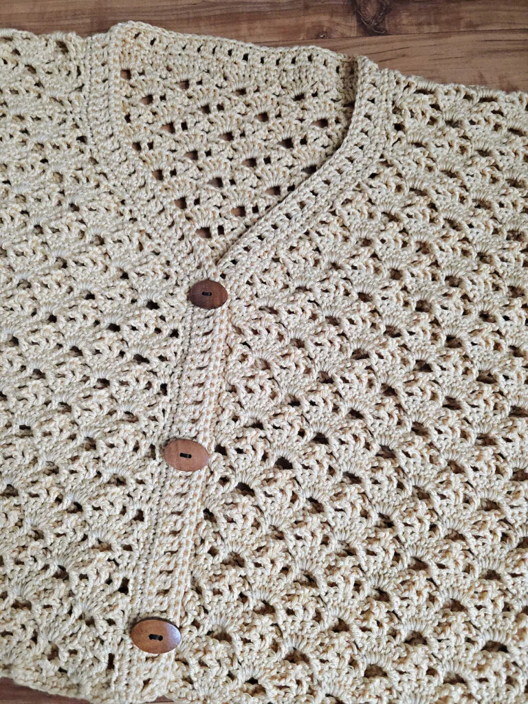 A beige colored cropped crochet cardigan against a wooden floor.
