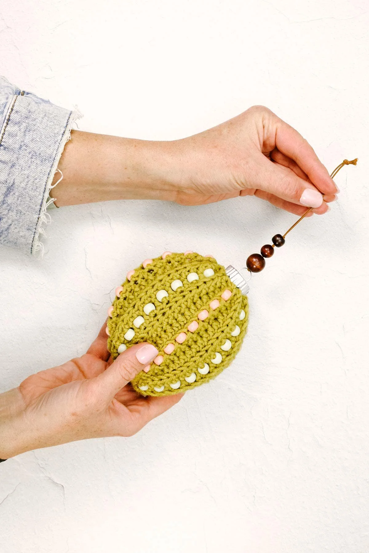 A green crochet ornament with pony beads held by a woman. 