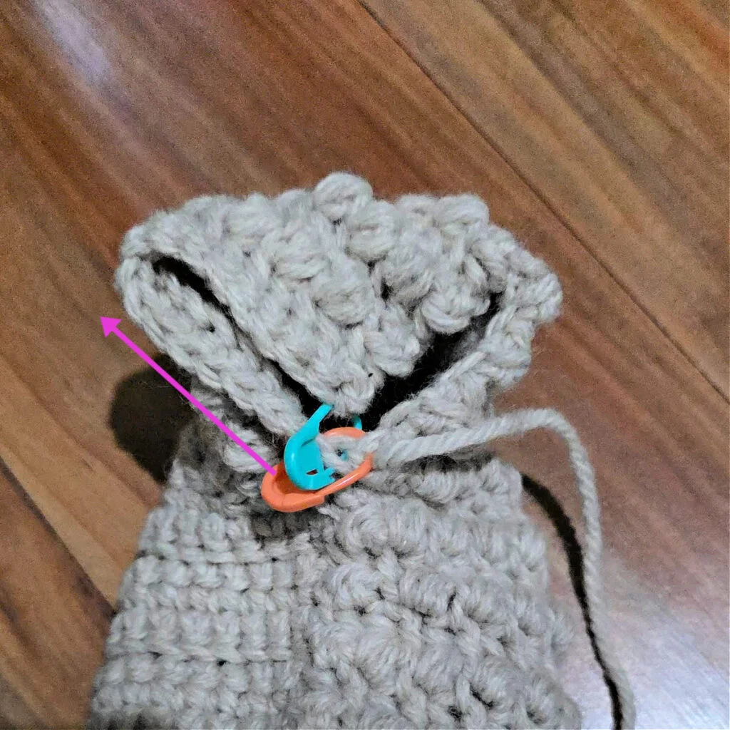 Seaming a grey crochet slipper against a wooden floor.