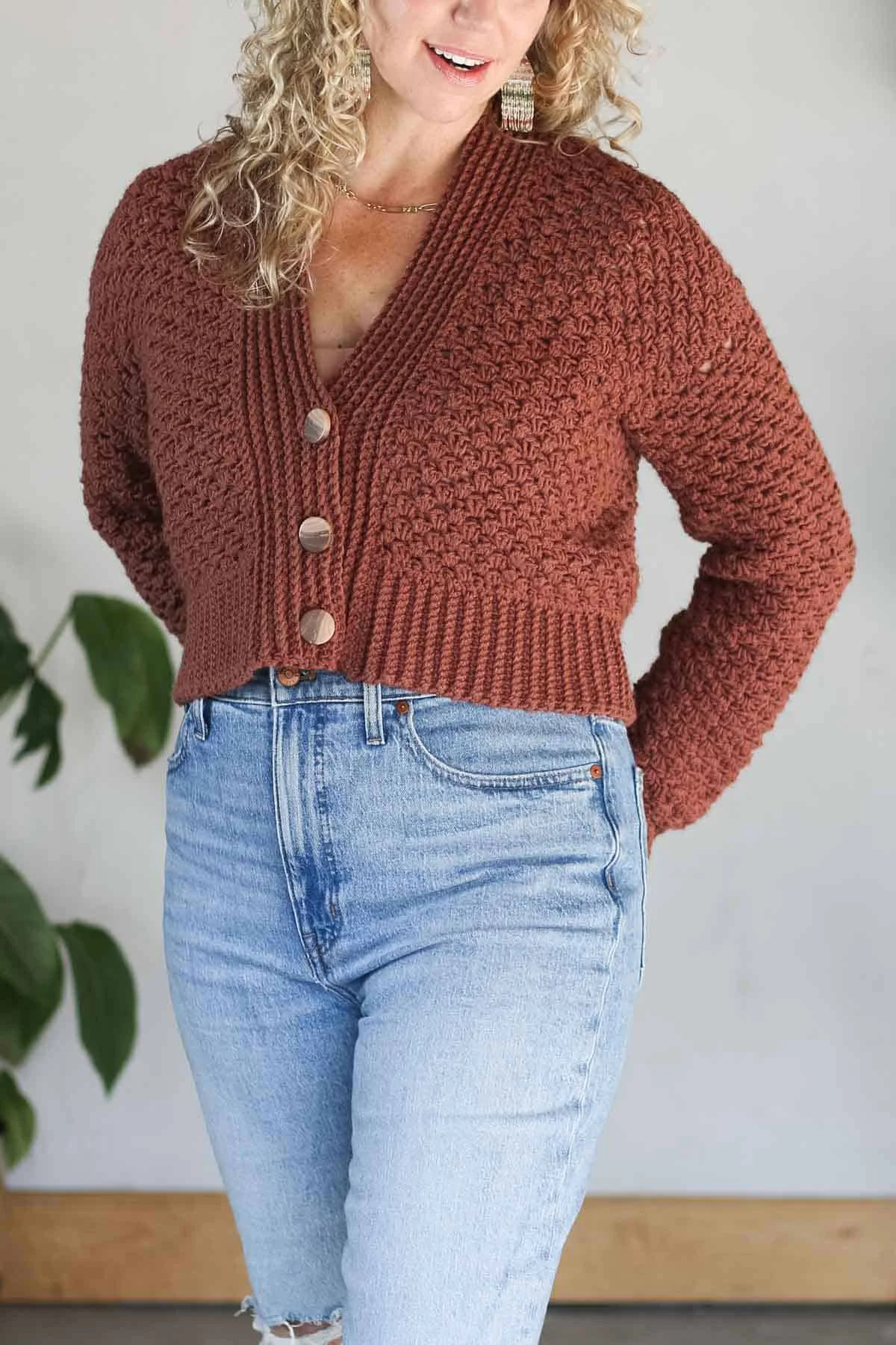 Close-up of a rust-colored half double crochet cardigan with wooden buttons, worn by Jess Coppom.