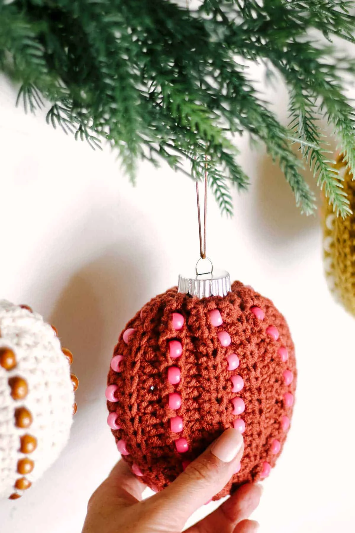 A rust colored crochet Christmas ornament with pony beads held by a woman.