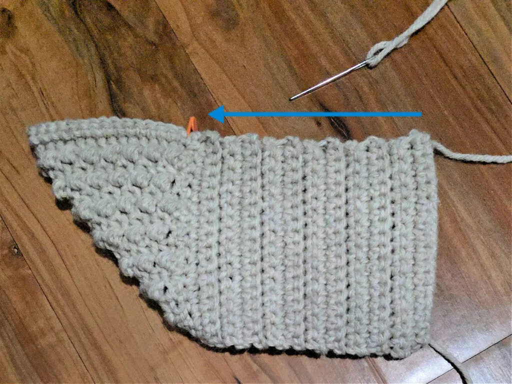 Seaming a grey crochet slipper against a wooden floor.