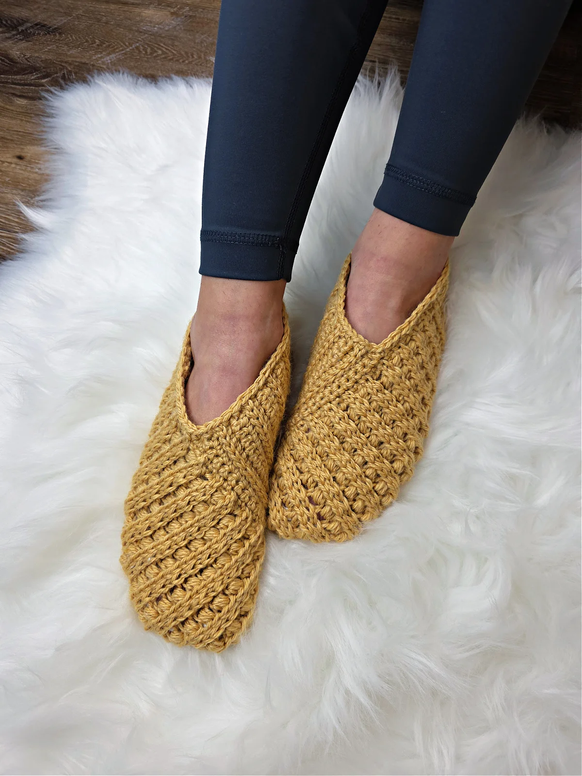 Model wearing mustard crochet slippers on feet and blue leggings.