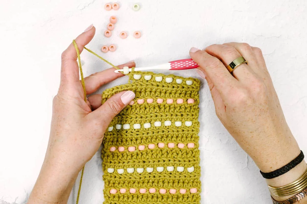 A woman inserting a pony bead into the crochet ornament pattern using a crochet hook.