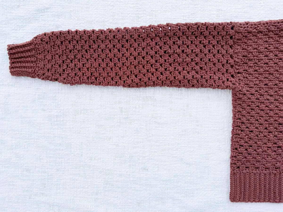 Flat lay of the cardigan body panel corner showing the ribbed hem and half double crochet stitch pattern in Lion Brand Color Theory yarn.